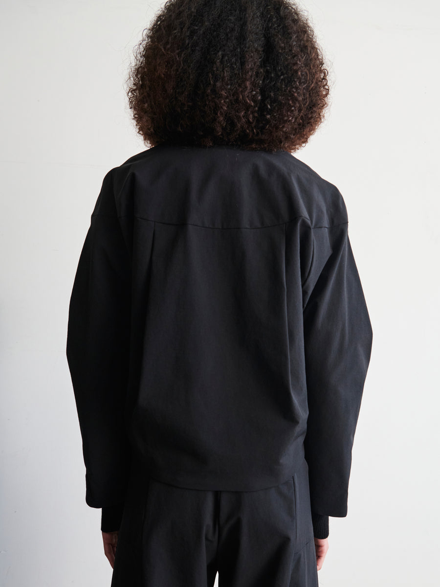 An individual with curly hair is wearing a contemporary T Bomber jacket by Zero + Maria Cornejo, featuring a two-way front zipper, seen from behind against a plain backdrop.