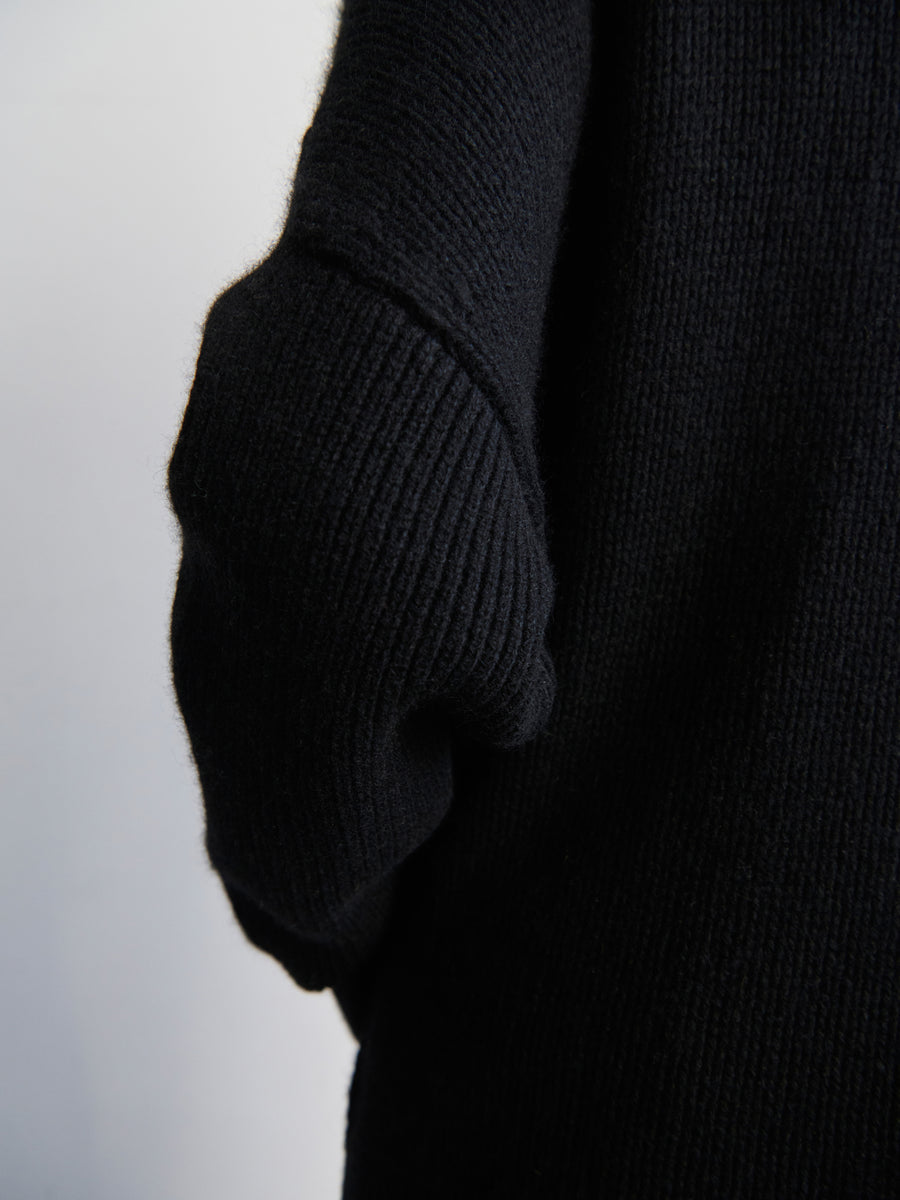 Close-up of the Long-Sleeved Rio Shrug by Zero + Maria Cornejo, featuring a black knitted sleeve with a textured, ribbed pattern that drapes softly from the oversized fit. The plain, light gray background accentuates the fabric's detail and rich recycled cashmere color.