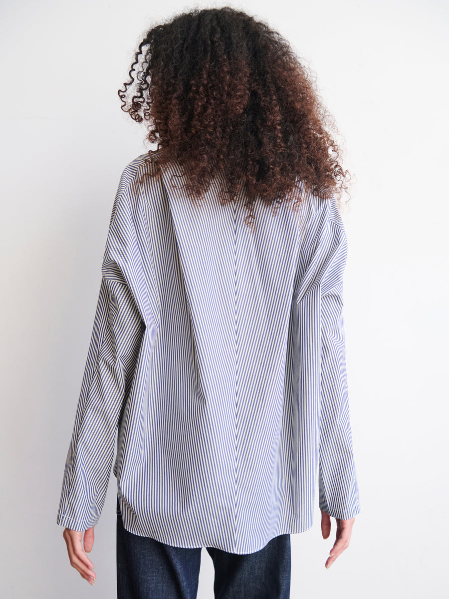 A person with curly hair, seen from behind, is wearing the oversized Long-Sleeved Fin Gaban Shirt by Zero + Maria Cornejo and dark pants, standing against a plain white background.