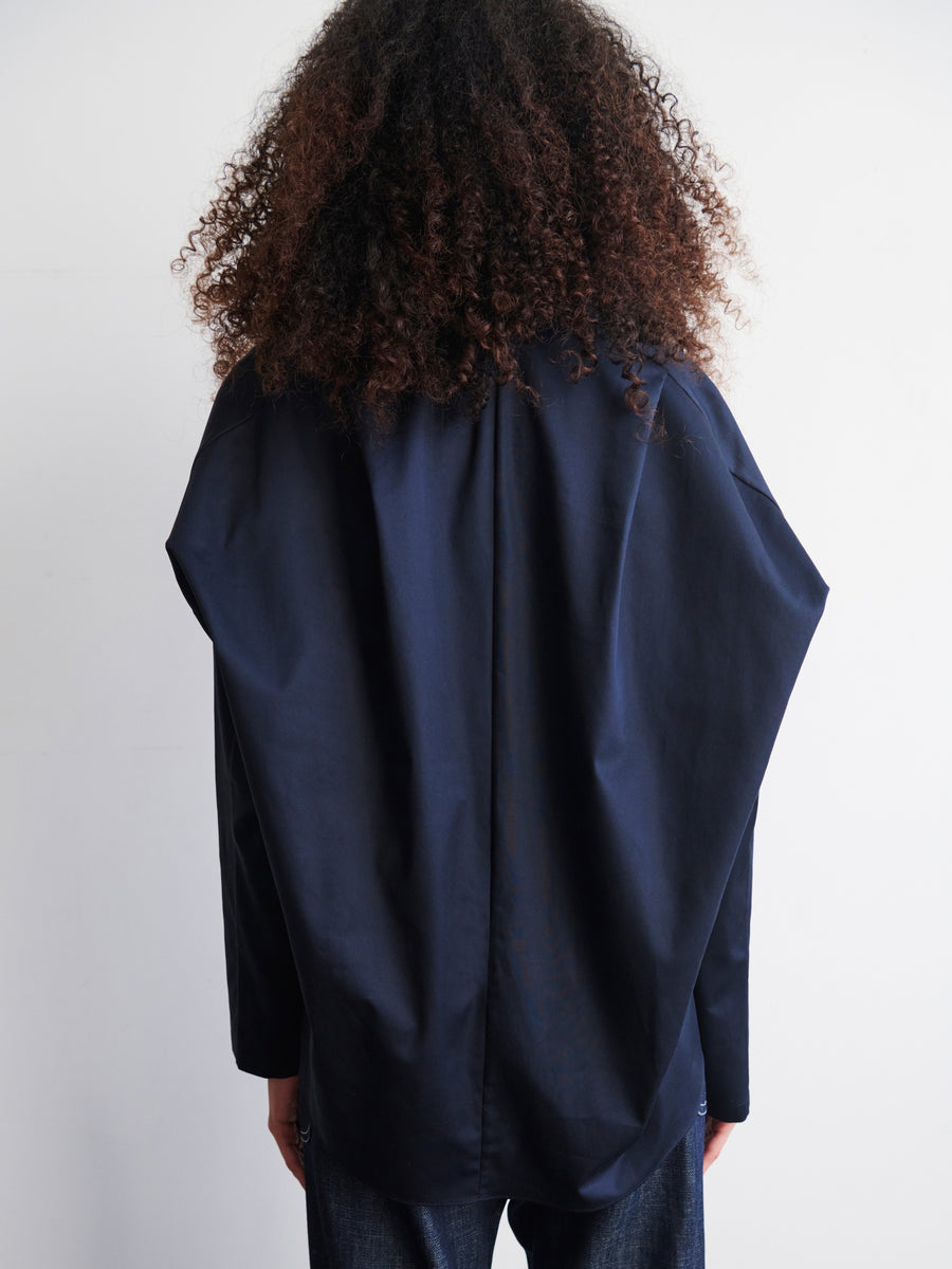 A person with curly hair is wearing a dark blue Long-Sleeved Fin Gaban Shirt by Zero + Maria Cornejo, featuring a subtle stand collar, viewed from the back against a plain white background.