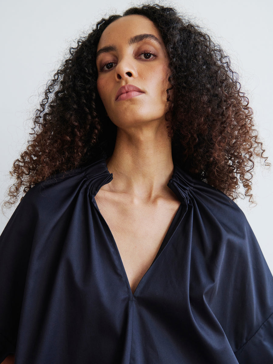 A person with curly hair, dressed in the Malia Shirt by Zero + Maria Cornejo, looks directly at the camera with a calm expression against a plain background.