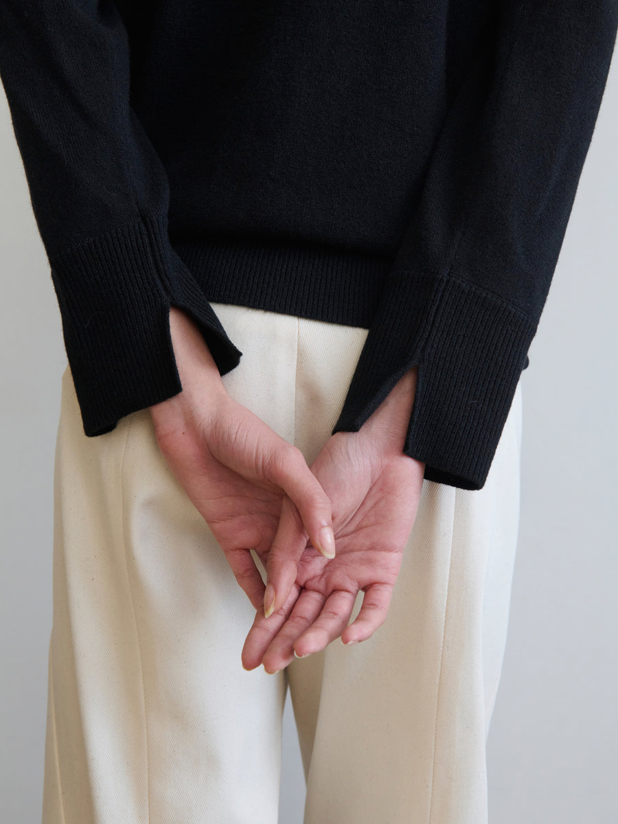 A person wearing a sustainably-sourced Knit Evi Top by Zero + Maria Cornejo in black and white pants stands with their hands clasped behind their back against a neutral background. Only the torso and hands are visible.