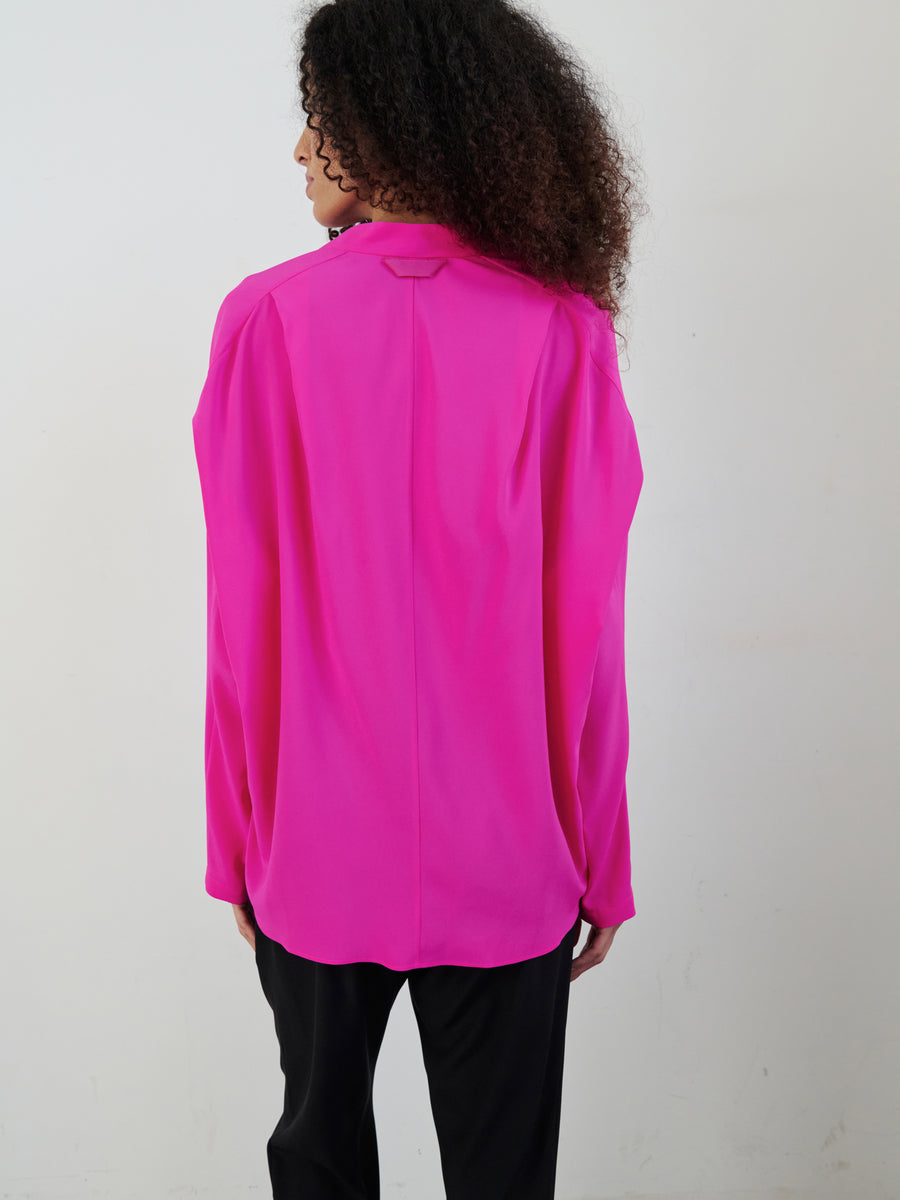 A person with curly hair stands with their back to the camera, wearing a Long-Sleeved Fin Gaban Shirt by Zero + Maria Cornejo and black pants, set against a plain background.