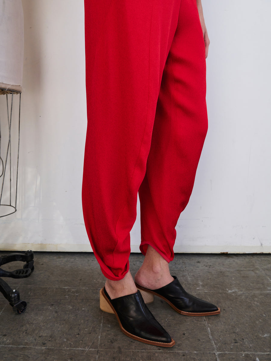 A person wearing the vibrant Takeo Pant by Zero + Maria Cornejo, crafted from sustainably-sourced woven viscose, pairs their look with black slip-on shoes featuring a low heel. They stand indoors on a concrete floor, with a partial view of an eco drape-covered metal stool visible on the left.