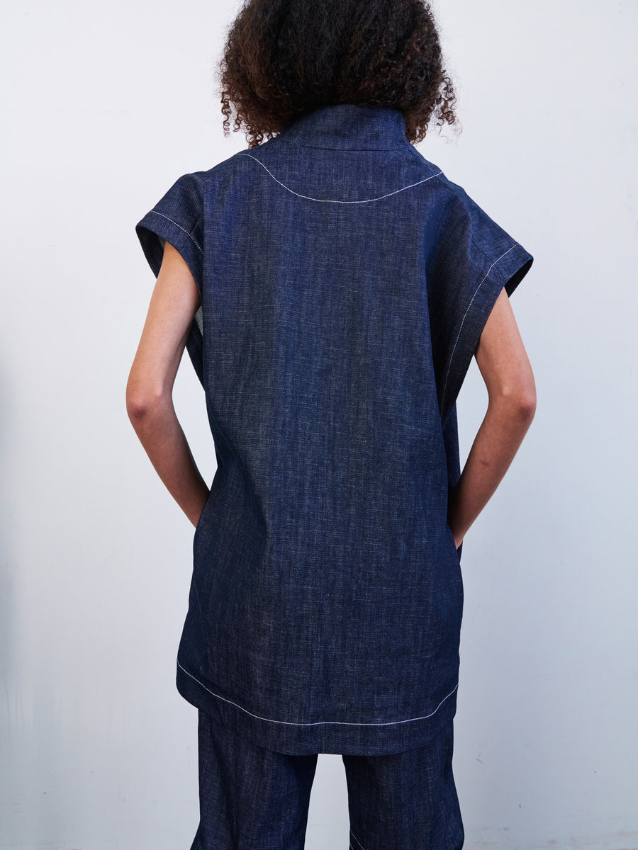 A person with curly hair is standing with their back to the camera, wearing the Ari Waistcoat and matching pants from Zero + Maria Cornejo, crafted from GOTS-certified organic denim cotton, against a plain light background.