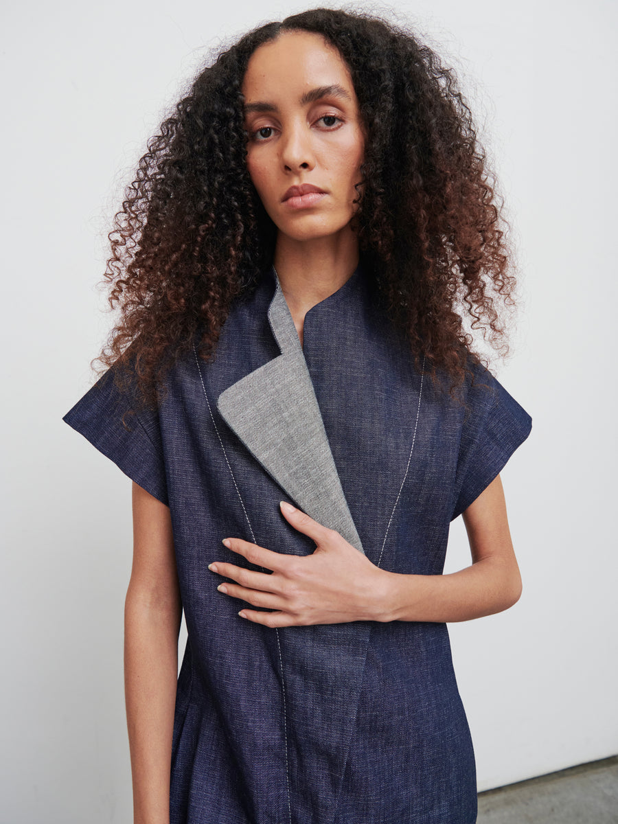 A person with long, curly hair wears an Edi Boiler Suit by Zero + Maria Cornejo, crafted from GOTS-certified organic cotton. They stand against a plain white background with a neutral expression and one hand resting on their chest.