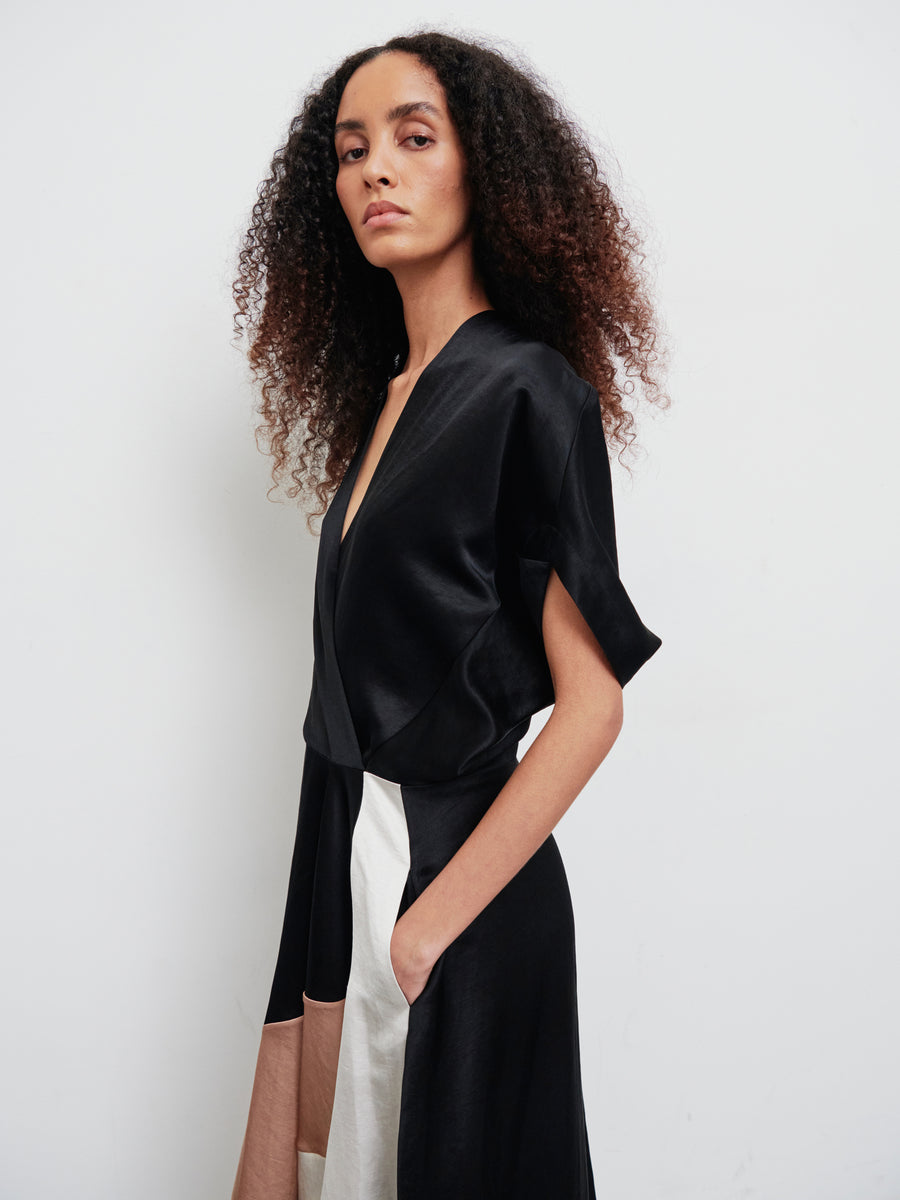 A woman with curly hair is wearing a stylish Patchwork Aki Wave Dress by Zero + Maria Cornejo, featuring an asymmetrical skirt. She stands against a plain white background, looking forward with a confident expression.