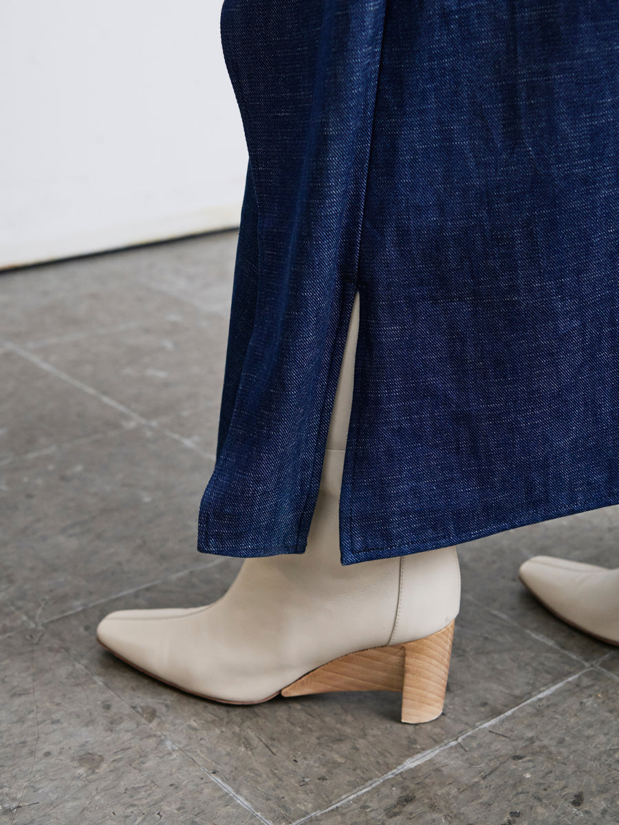 Close-up of a person wearing the Mido Dress by Zero + Maria Cornejo, crafted from Cradle 2 Cradle Certified fabric, paired with beige heeled boots featuring wooden soles. The image captures the lower leg and footwear on a stone floor.