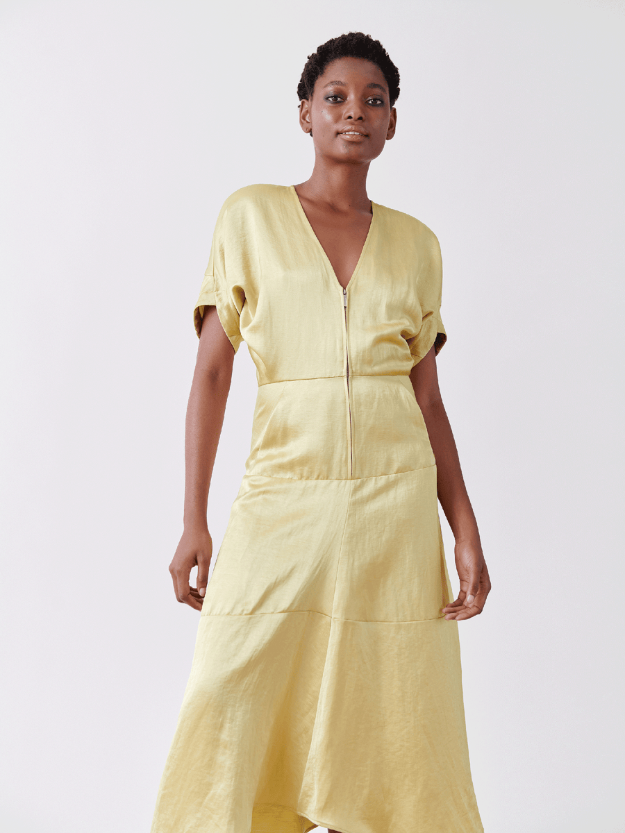 A person with short hair is wearing the Aissa Joi Dress from Zero + Maria Cornejo. This light yellow linen-blend dress features an A-line skirt, V-neck, and short sleeves, with a waist seam and below-knee length. They stand against a plain white background.