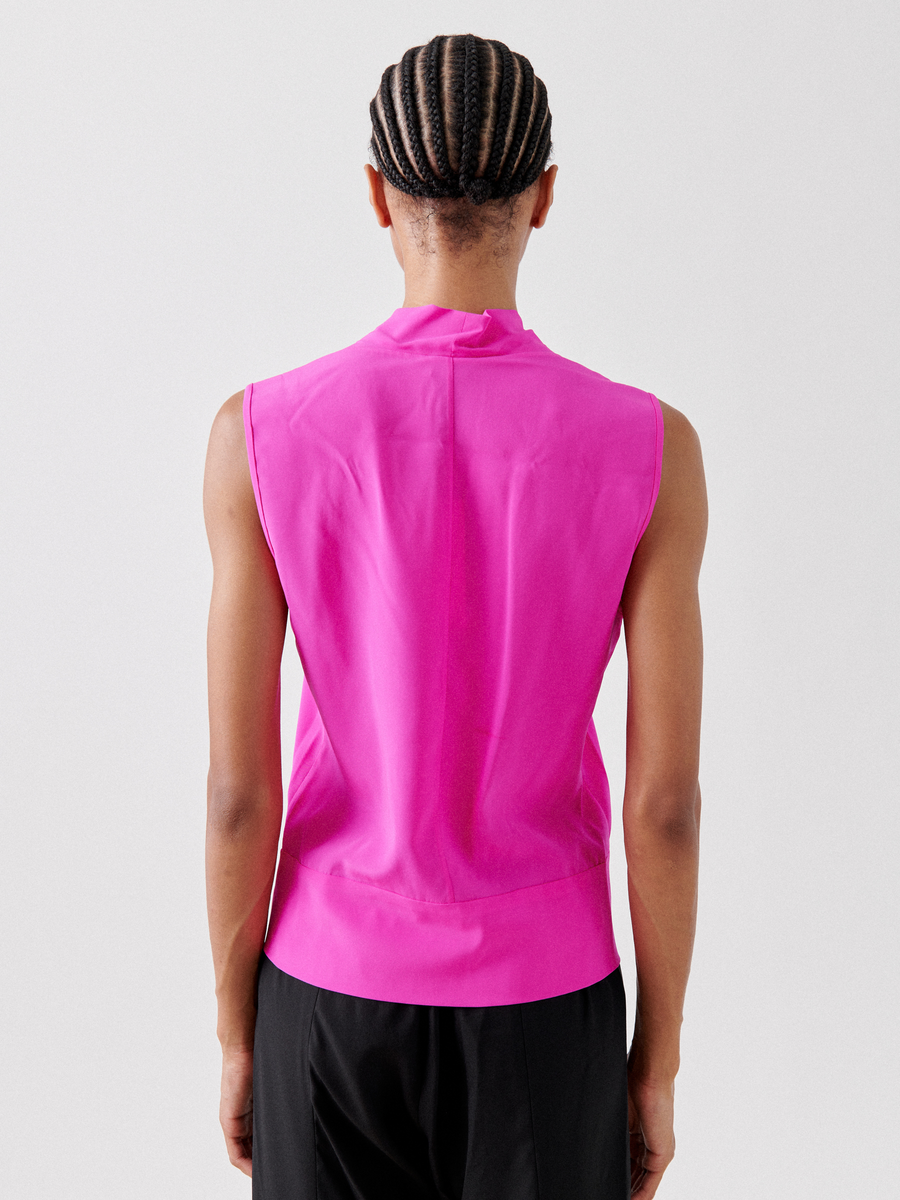 A person with braided hair, facing away, wears the Sacha Top - Final Sale by Zero + Maria Cornejo in bright pink silk charmeuse, paired with black pants against a plain white background.