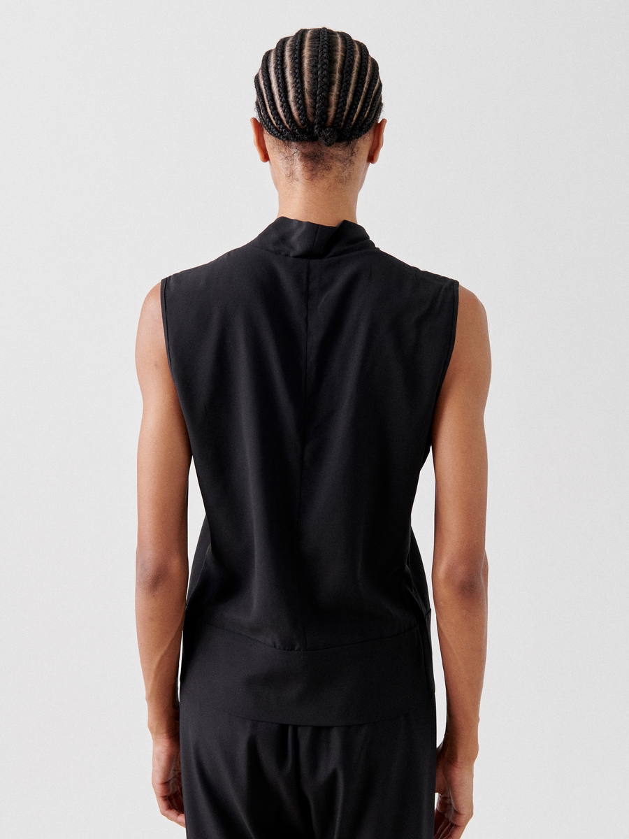 Person standing with back facing the camera, showcasing a sleeveless v-neckline Sacha Top from Zero + Maria Cornejo and black braided hair. The background is plain white.