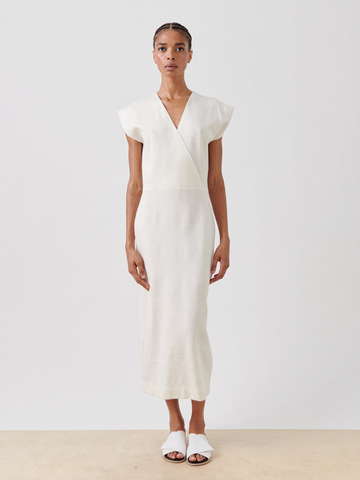 Against a white backdrop, they wear the Wrap Mido Dress by Zero + Maria Cornejo. The off-white v-neck dress, crafted from eco-friendly cotton-modal jersey with cap sleeves, pairs perfectly with white slide sandals and neatly styled hair.