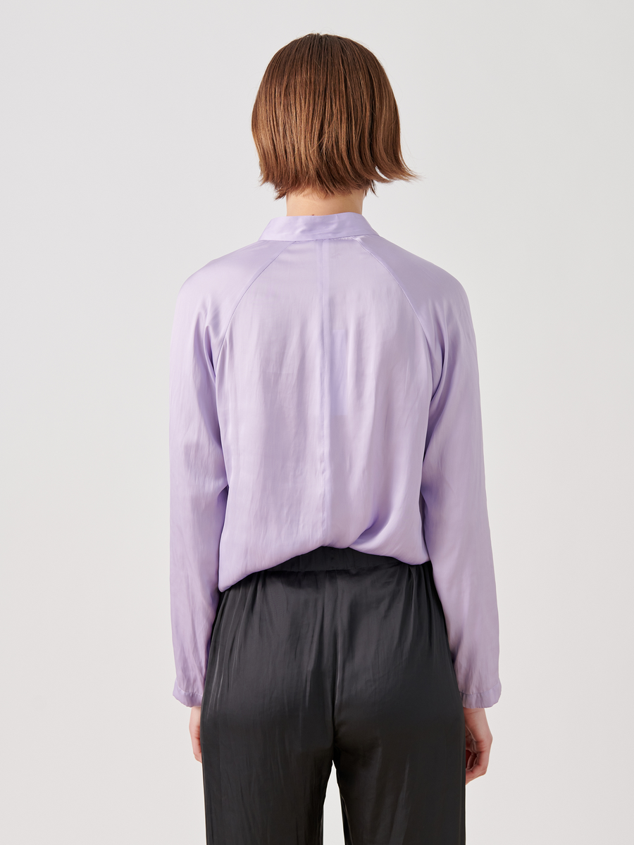 A person with short brown hair is seen from the back wearing a Long-Sleeved Evi Top by Zero + Maria Cornejo in light purple and black pants, set against a plain white background.