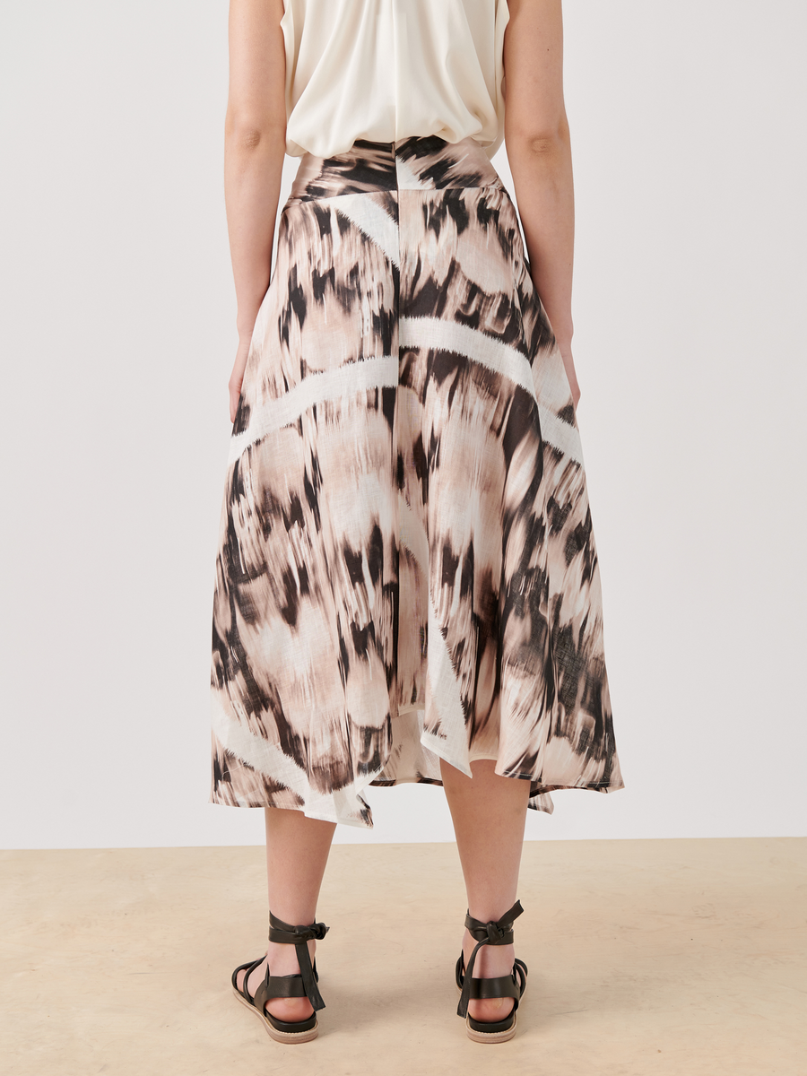 A person wearing the Zero + Maria Cornejo Aki Wave Skirt - Final Sale, a flowing multicolor print midi skirt created with digital inkjet printing, stands with their back to the camera. They pair it with a light blouse and black strappy sandals against a neutral background.