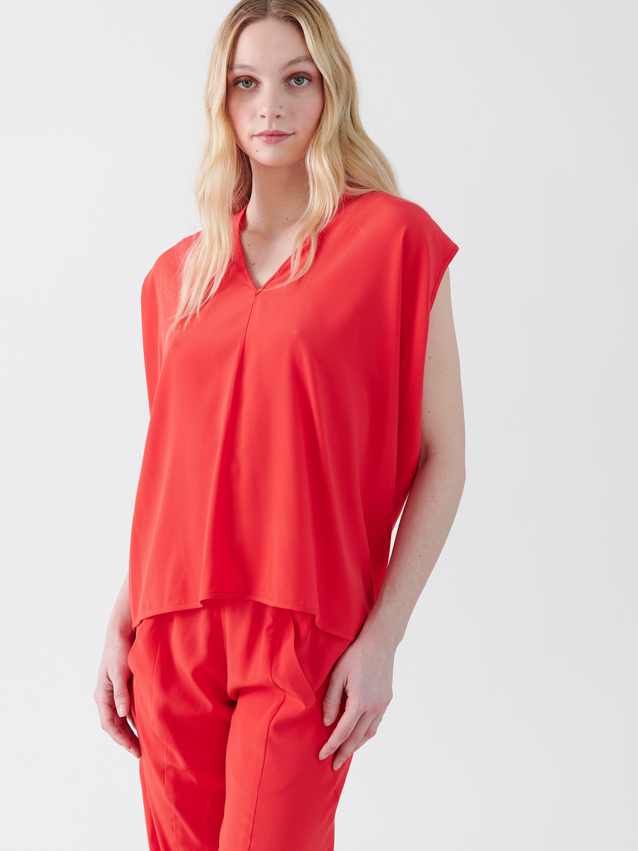 A person stands against a plain white background, wearing the bright red Ina Tank by Zero + Maria Cornejo and matching pants. Their long blonde hair cascades down as they look directly at the camera.