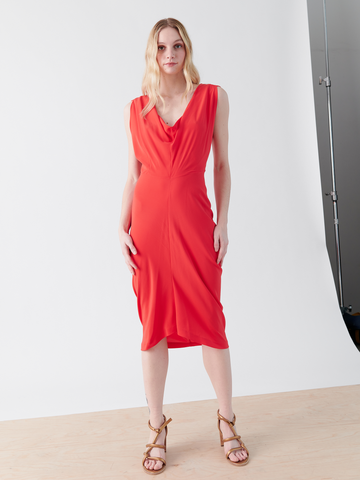 A person with long blonde hair is wearing the Zero + Maria Cornejo Siren Dress - Final Sale, a sleeveless, knee-length silk charmeuse dress, paired with strappy sandals. They are standing on a wooden floor against a plain, white background.