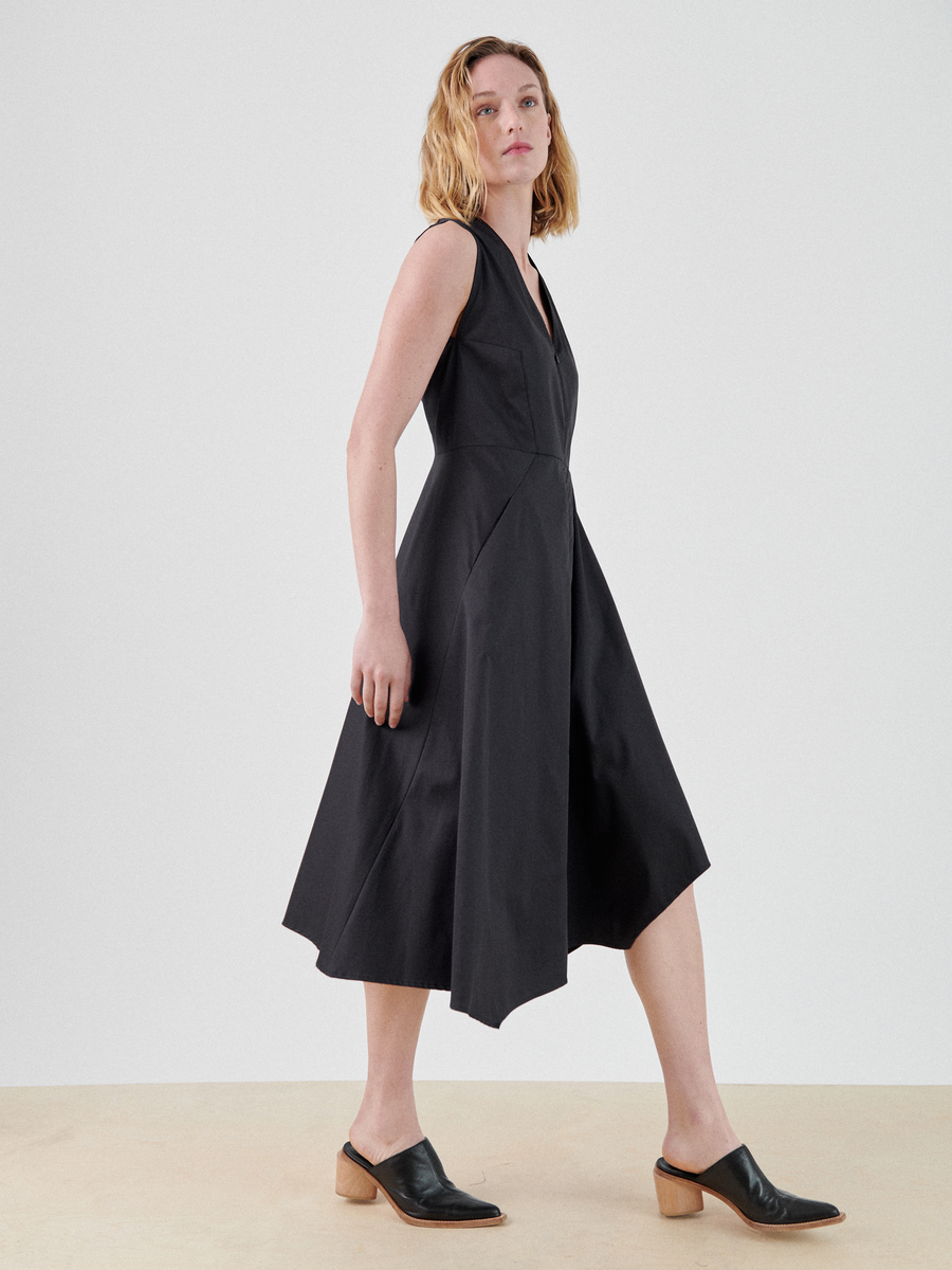 A person with shoulder-length wavy blonde hair is wearing a Zero + Maria Cornejo Sleeveless Wave Dress. They have on black mule shoes with a low wooden heel. They stand against a plain light background, looking to the side.