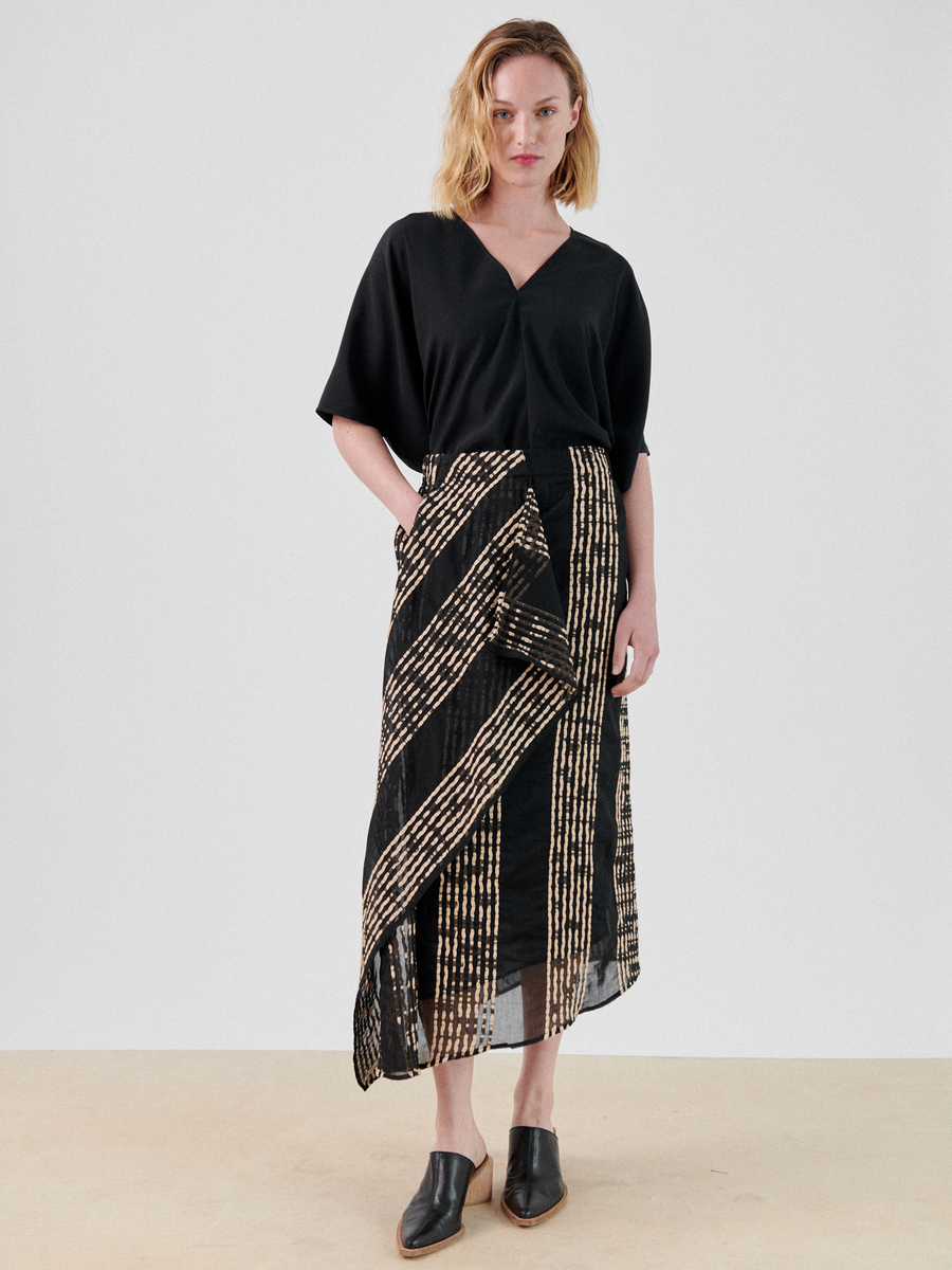 A woman in a black shirt and the One Skirt by Zero + Maria Cornejo, made from organic cotton with an asymmetrical ruffle, perfect for a summer staple.