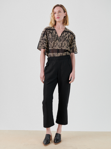 A woman with shoulder-length blonde hair stands against a plain white background. She is wearing a TENCEL™ Lyocell black and beige patterned short-sleeve blouse, Zero + Maria Cornejo Eko Pant, and black slip-on shoes. She has a neutral expression and her arms are relaxed by her sides.