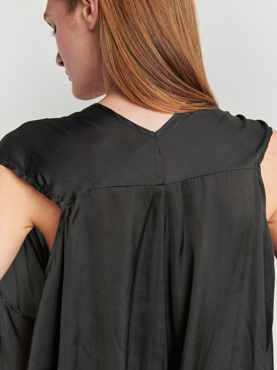 A person with long, straight, light brown hair is photographed from the back, wearing the Ina Tank by Zero + Maria Cornejo. This sleek sleeveless V-neck top is made from recycled polyester and features a silky sheen. The image focuses on the upper part of the person's back and shoulders.