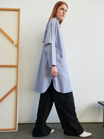 Wearing the Zero + Maria Cornejo Biker Shirt Dress, a person with long hair stands indoors beside an unframed canvas leaning against a neutral white wall.