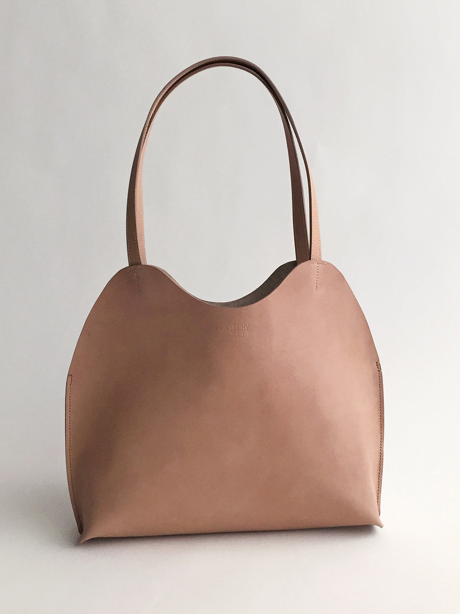 The Bartleby Objects Freja Tote, a taupe leather bag with a minimalist design, features two handles and a simple, smooth finish, expertly handmade in New York City.