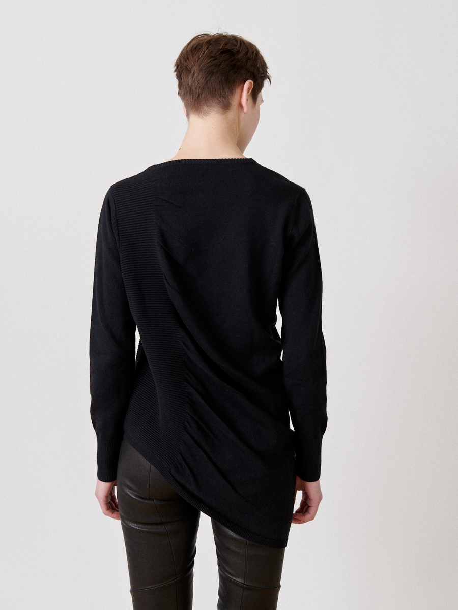 A person with short hair is standing with their back to the camera, wearing the Zero + Maria Cornejo Off Kilter Tunic and black leather pants. The background is plain and light-colored.