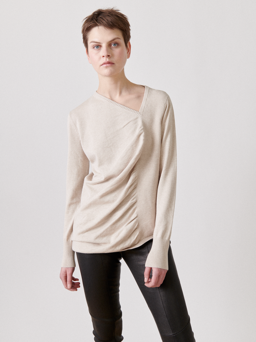 A person with short, brown hair stands against a plain white background. They are wearing the Zero + Maria Cornejo Off Kilter Tunic, paired with black leather pants. They have a neutral expression and one hand in their pocket.