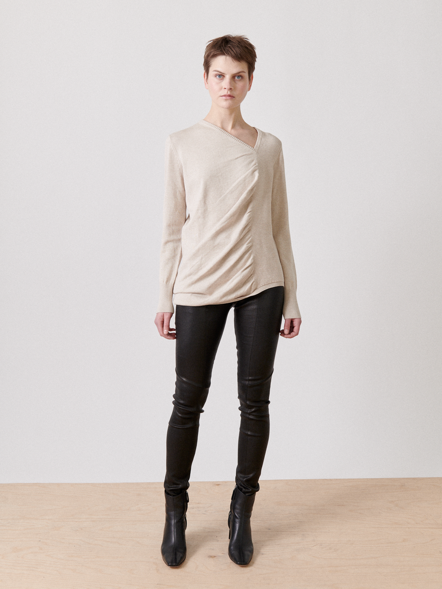 A person stands against a plain background, wearing the Off Kilter Tunic by Zero + Maria Cornejo, black leather pants, and black ankle boots. The person has short brown hair and a neutral facial expression, standing with arms relaxed by their sides.