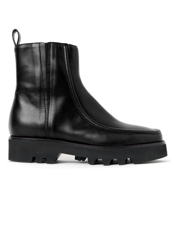 A black nappa leather Moccasin Boot with a chunky sole and a slight heel from Zero + Maria Cornejo. The boot, made in Italy, features an above-ankle height and a pull tab at the back. It has a sleek finish with minimal stitching and a rounded-square toe. The rugged tread pattern on the sole adds extra grip.
