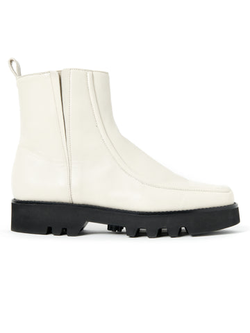 A single white nappa leather Moccasin Boot by Zero + Maria Cornejo with a smooth finish, featuring a thick black rubber sole with a rugged tread. The boot, made in Italy, has a pull tab at the back and minimal stitching for a sleek, modern look with a rounded-square toe.