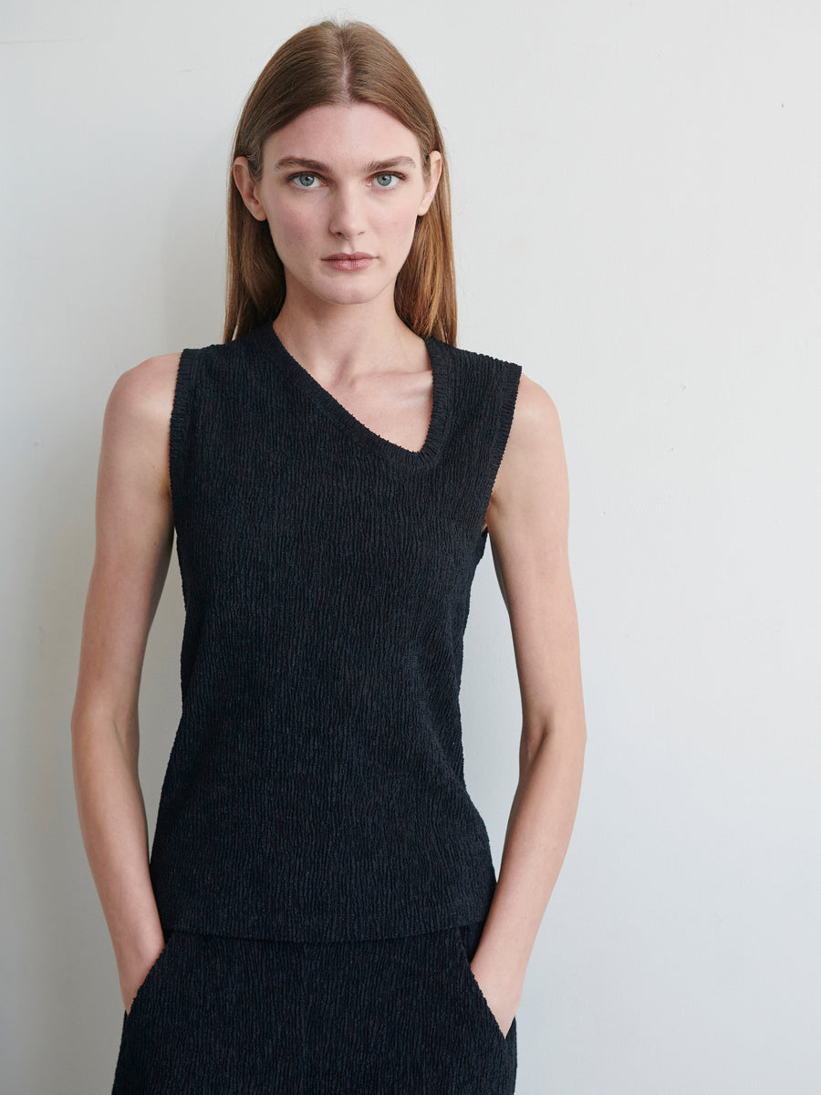 A woman with long straight hair stands against a plain white background. She is wearing the Off Kilter Tank made from eco boucle fabric by Zero + Maria Cornejo and has her hands in her pockets. Her expression is neutral, and she is looking directly at the camera.