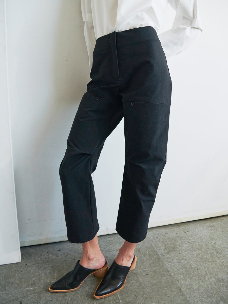 Person wearing black Biker Pants by Zero + Maria Cornejo and black pointed-toe mules, with a white shirt. The photo is cropped to show from the white shirt's cuffs down to the feet, standing on a grey textured floor against a plain white background. A premium New York made product.