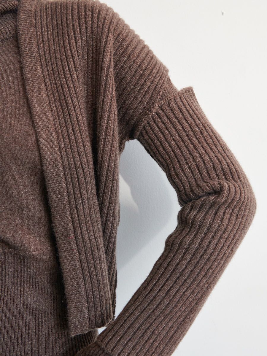 A close-up of the Slash Ani Cardigan by Zero + Maria Cornejo, a brown ribbed knit design in recycled cashmere, draped over one shoulder against a plain white background. The layering creates an overlapping effect on the sleeve and shoulder.