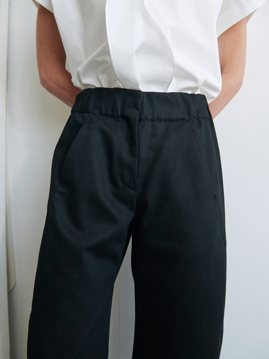 Person wearing a white shirt tucked into high-waisted Aissa Cargo Pants by Zero + Maria Cornejo standing against a light-colored wall. The image focuses on the midsection, showcasing the details of the clothing.