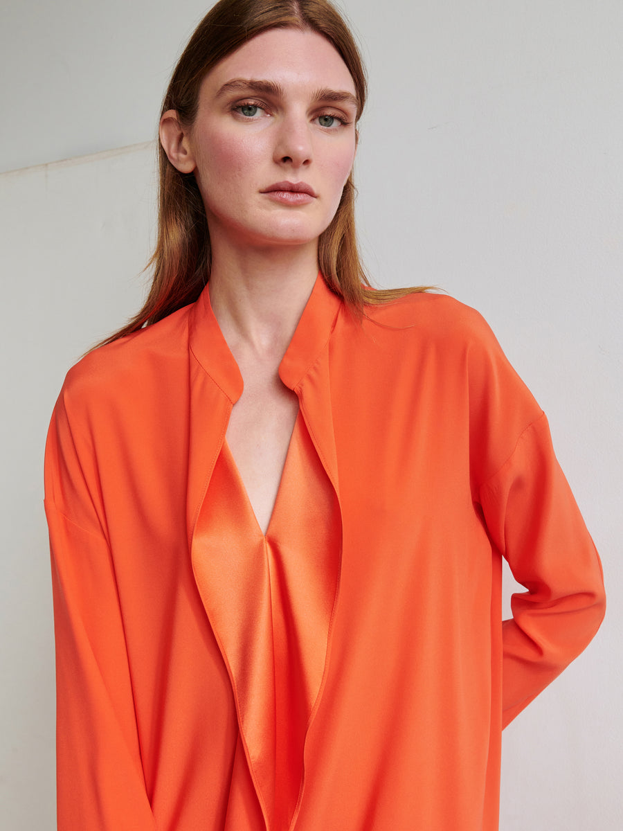 A person with long light brown hair stands against a plain background, wearing the Zero + Maria Cornejo Long-Sleeved Fin Gaban Dress. They have a neutral expression and are looking slightly off camera.