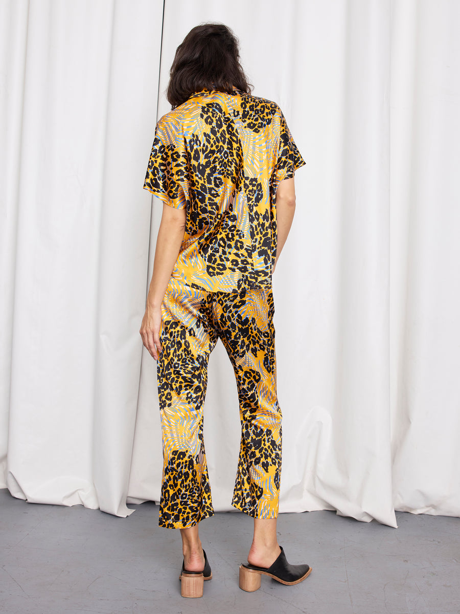 A person faces away from the camera, wearing Zero + Maria Cornejo’s Eko Pant—an abstract animal print silk trouser with an elastic waist—paired with a matching short-sleeve top and heeled mules. Their hair is loose; white curtains hang behind. Made in New York.