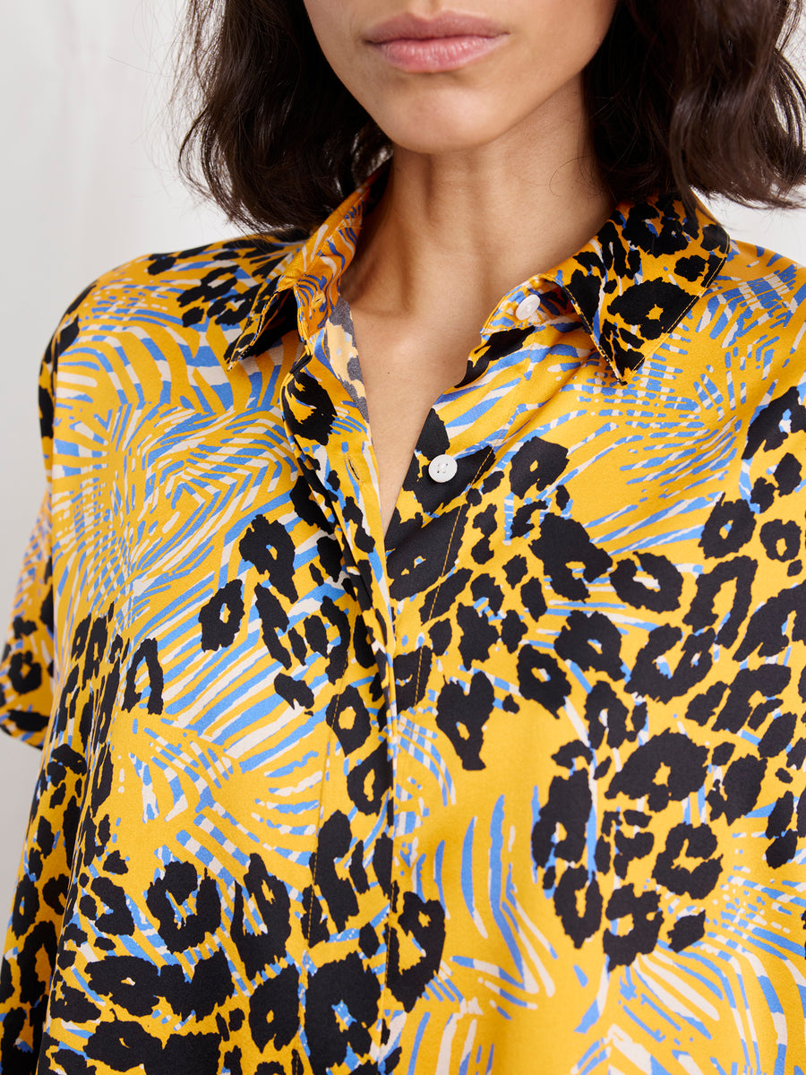 A woman wears the Zero + Maria Cornejo Circle Shirt, featuring an abstract animal print in bold yellow, black, and blue. Her face is partially visible and her dark hair falls in loose waves.