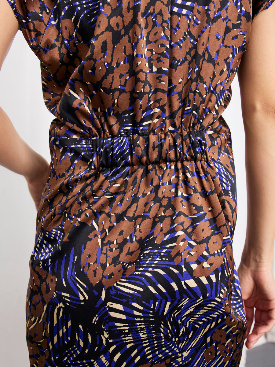 Close-up of a person wearing the Ruched Stella Dress by Zero + Maria Cornejo—a silk, knee-length dress with brown, black, and blue abstract animal print and ruched waist detailing. The wearer’s arm is visible on the right.