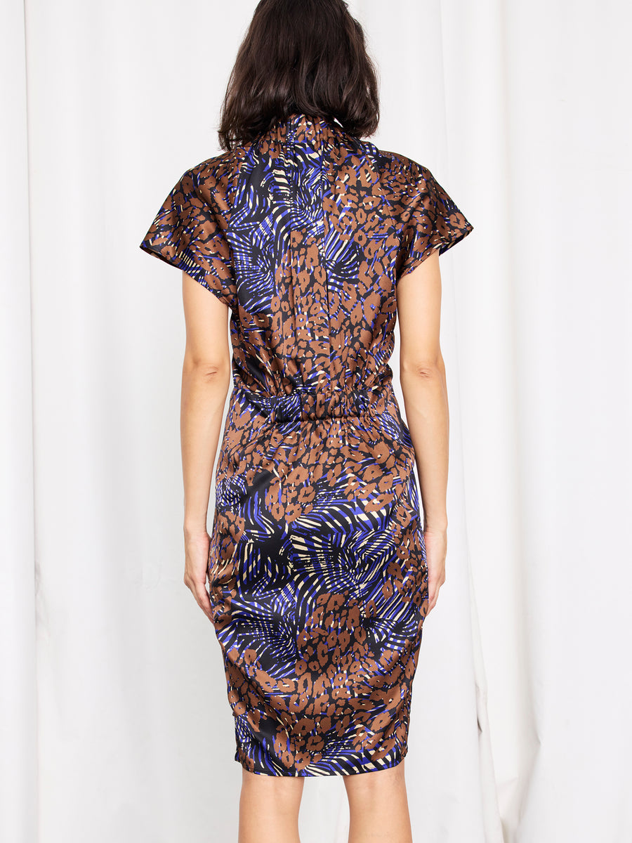 A woman faces away in the Ruched Stella Dress by Zero + Maria Cornejo, a silk knee-length piece featuring a brown, blue, and black abstract animal print on white.