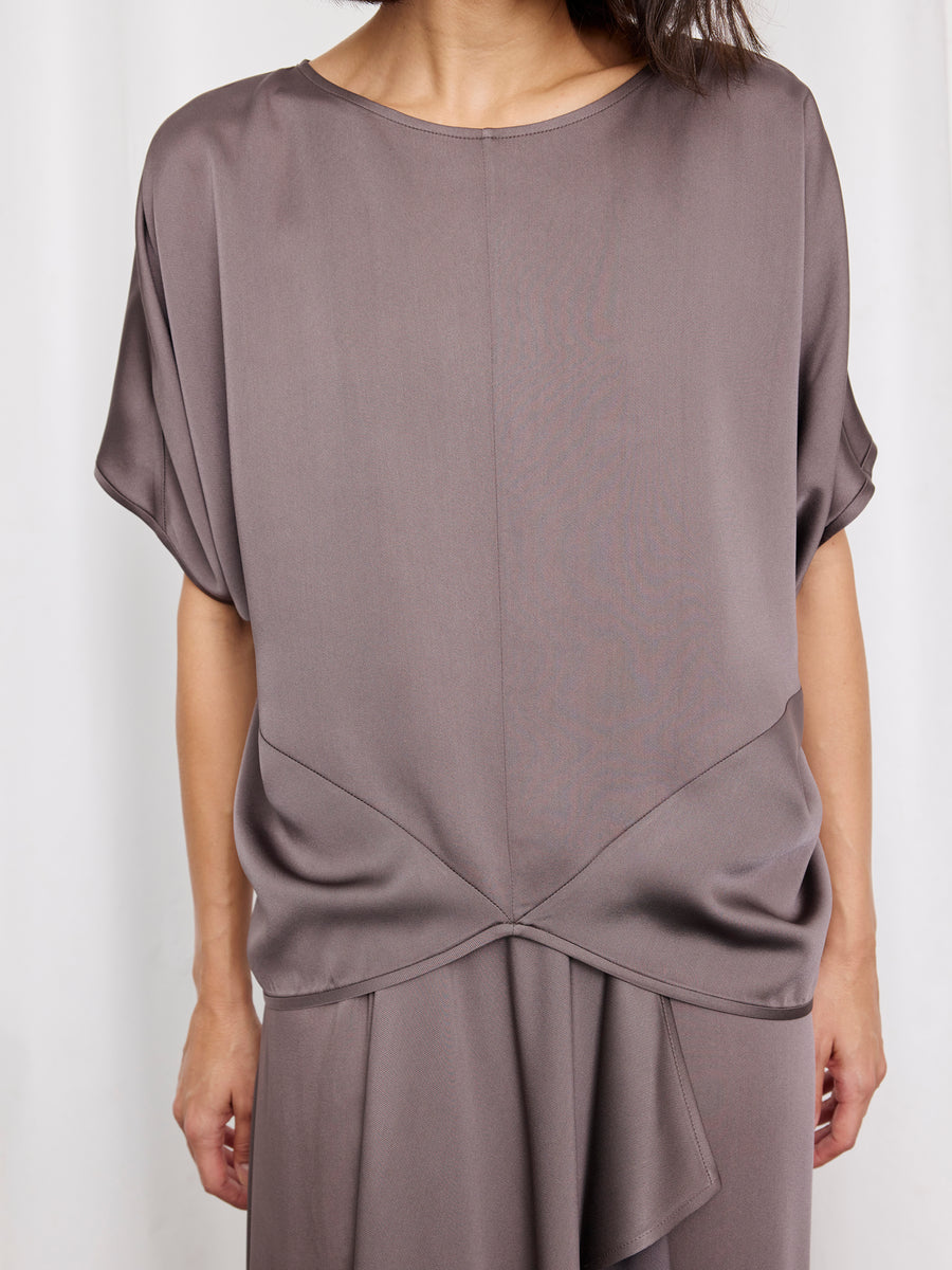 A person wears the mauve Rio Top by Zero + Maria Cornejo, a woven draped cap-sleeve style with gathered waist detail, paired with a matching skirt. The photo shows the outfit from shoulders to mid-thigh. Made in New York.