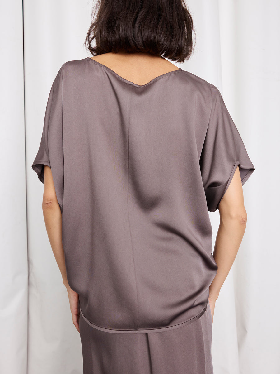 A person with chin-length dark hair, seen from behind, wears the Rio Top by Zero + Maria Cornejo with cap sleeves and a matching skirt, made in New York, standing before white curtains.