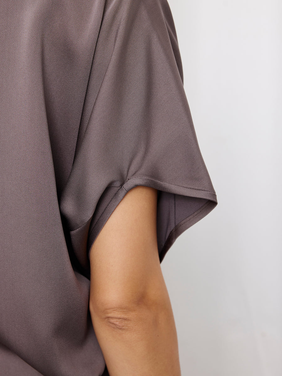 A close-up shows a person's arm and shoulder wearing the grayish-purple Rio Top by Zero + Maria Cornejo, featuring woven fabric and cap sleeves. The image highlights the sleeve and upper arm against a light background.
