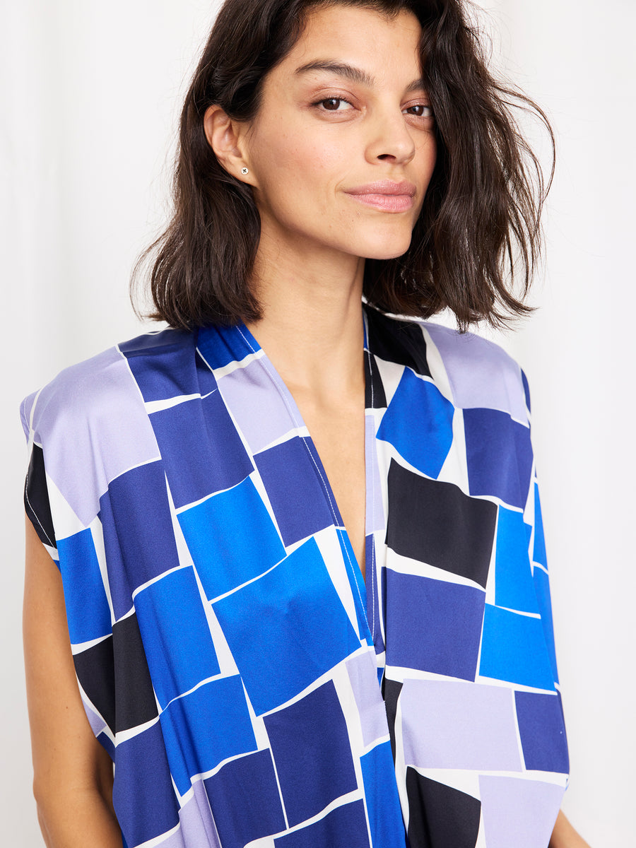 A woman with shoulder-length dark hair models the Issa Dress by Zero + Maria Cornejo, a knee-length piece featuring bold blue, black, and white geometric graphics, standing against a plain white background and offering a subtle smile.