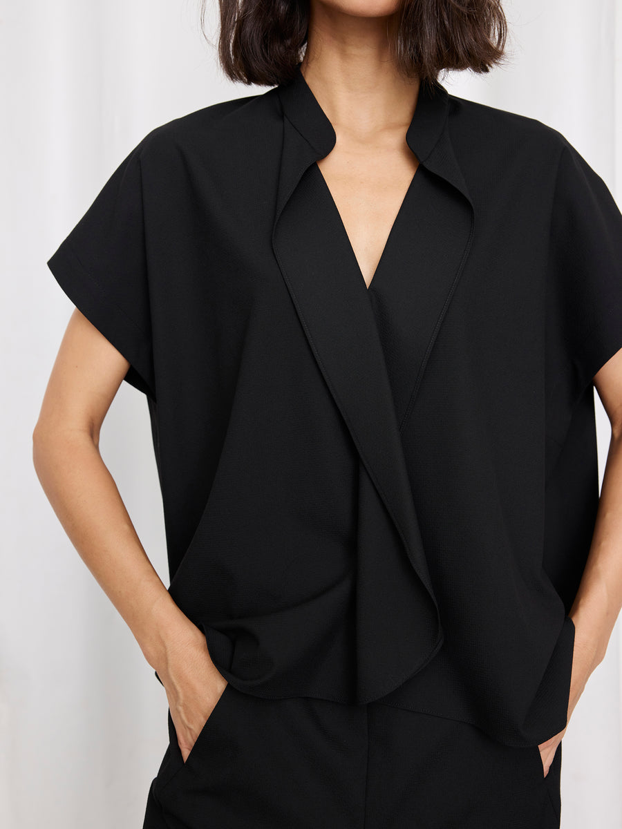A person wearing the loose-fitting, short-sleeved Fin Gaban Shirt by Zero + Maria Cornejo, featuring an open collar, stands with one hand in their pocket against a white background.