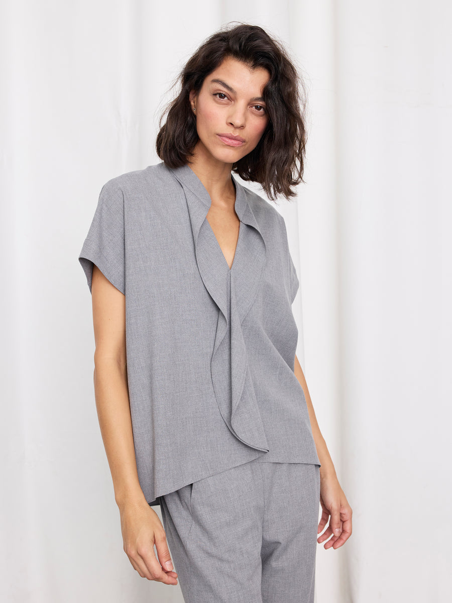 A woman with shoulder-length dark hair wears the Fin Gaban Shirt by Zero + Maria Cornejo, featuring a textured weave and draped front, paired with matching pants, standing against a white background.