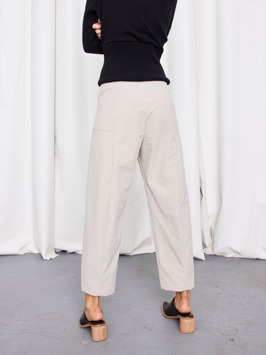 A person stands facing away, wearing the Zero + Maria Cornejo Margot Pant with a black long-sleeve top and open-toe sandals, against a backdrop of white curtains and a gray floor.