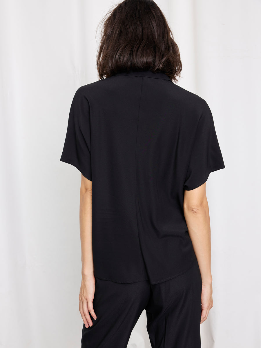 A person with shoulder-length dark hair, seen from behind, wears the Zero + Maria Cornejo Circle Shirt and matching black pants, made in New York, standing against a plain white background.