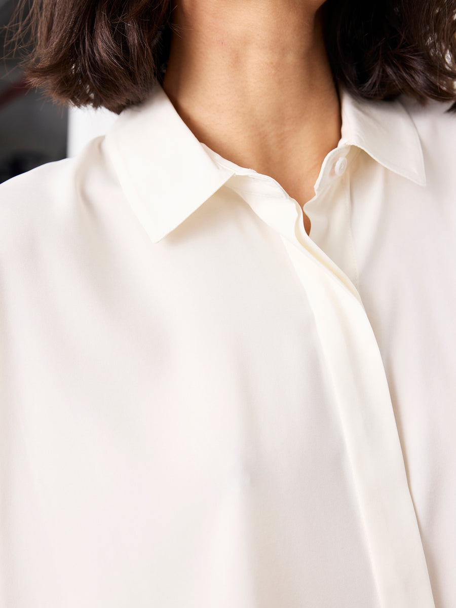 Close-up of a person in the Zero + Maria Cornejo Circle Shirt, a white, short-sleeved silk top with a refined neckline. Brown, chin-length hair partly obscures the face. Effortlessly sophisticated and made in New York.