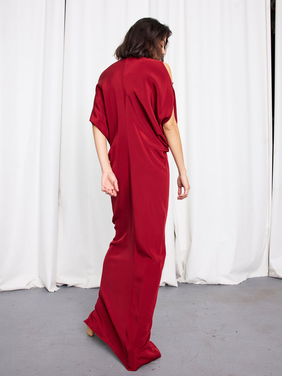 Wearing the Long Miu Dress by Zero + Maria Cornejo, a person with shoulder-length dark hair stands with their back to the camera in front of white curtains on a gray floor.